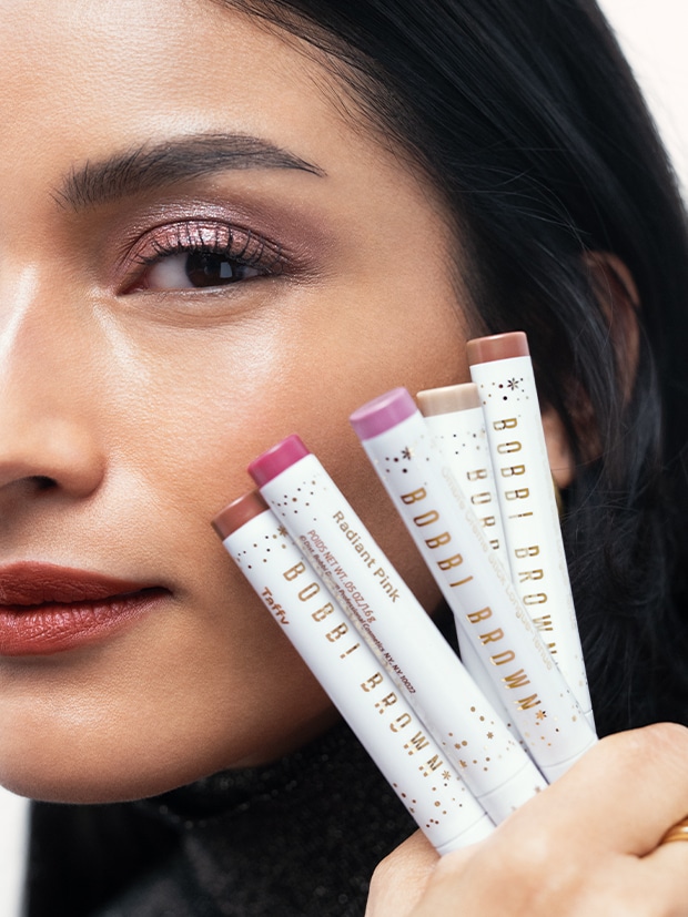 Model holding Long-Wear Cream Shadow Sticks in limited edition shades for Holiday