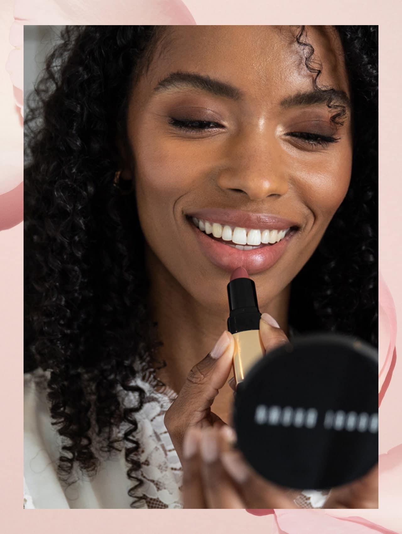 Imagine containing step 5 model applying lipstick, smiling while looking into compact Bobbi Brown mirror