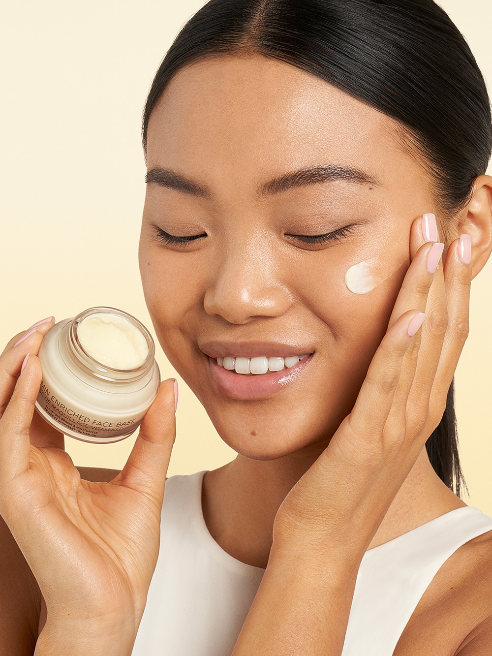 Close up of smiling model applying Vitamin Enriched Face Base to skin, with a focus on application